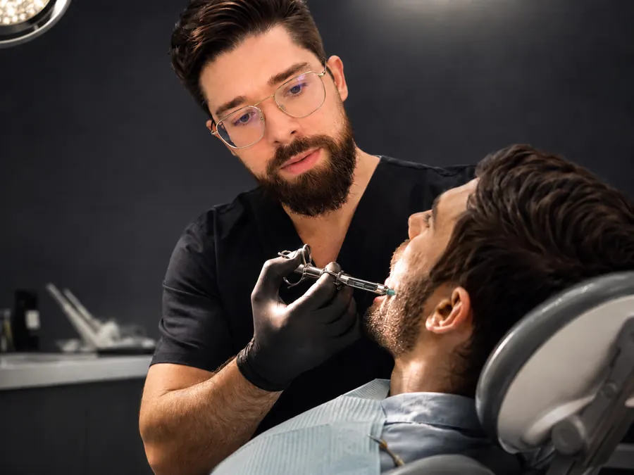 Profesional de odontología aplicando anestesia mandibular en un paciente reclinado